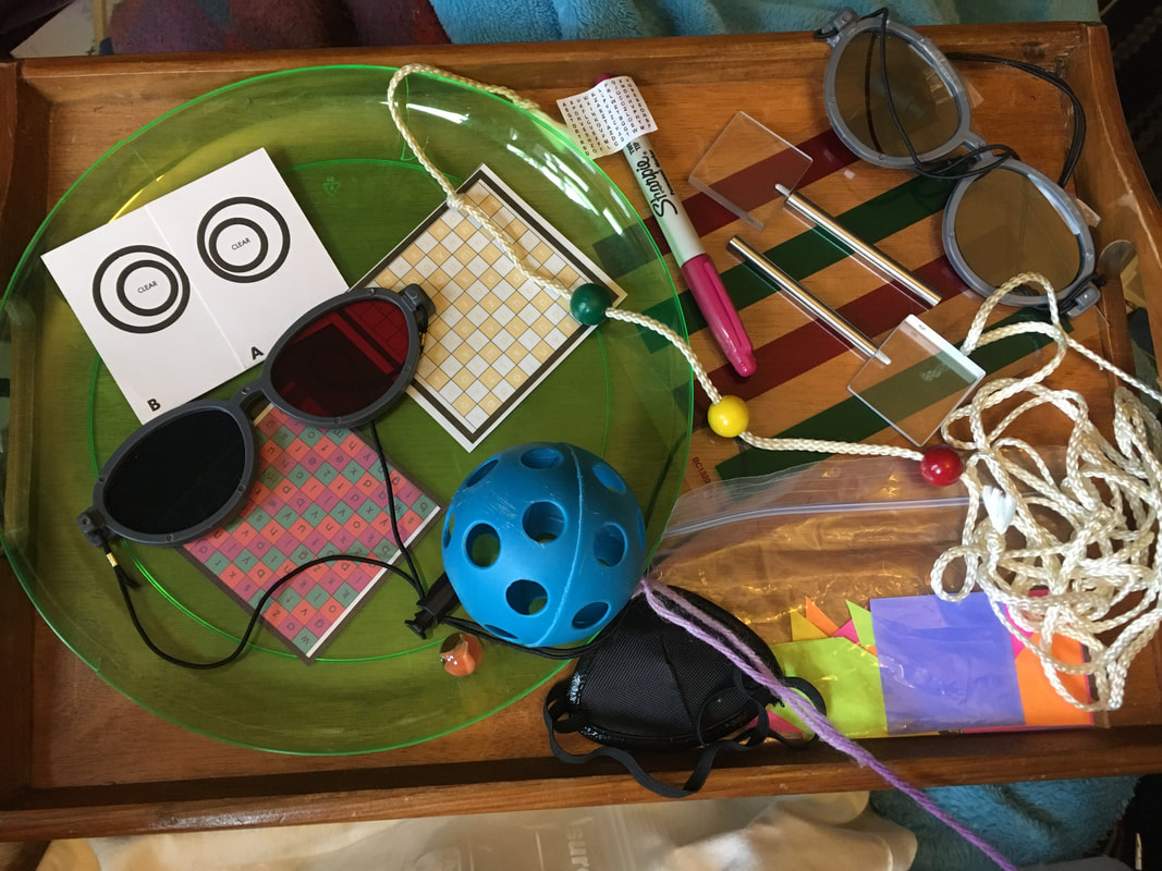Assortment: Plastic plate with marble, small grids with letters and different colors, red/blue glasses, a long string with 3 different color beads on it, a ball, prisms on sticks, small pieces of paper in different shapes, an eyepatch 