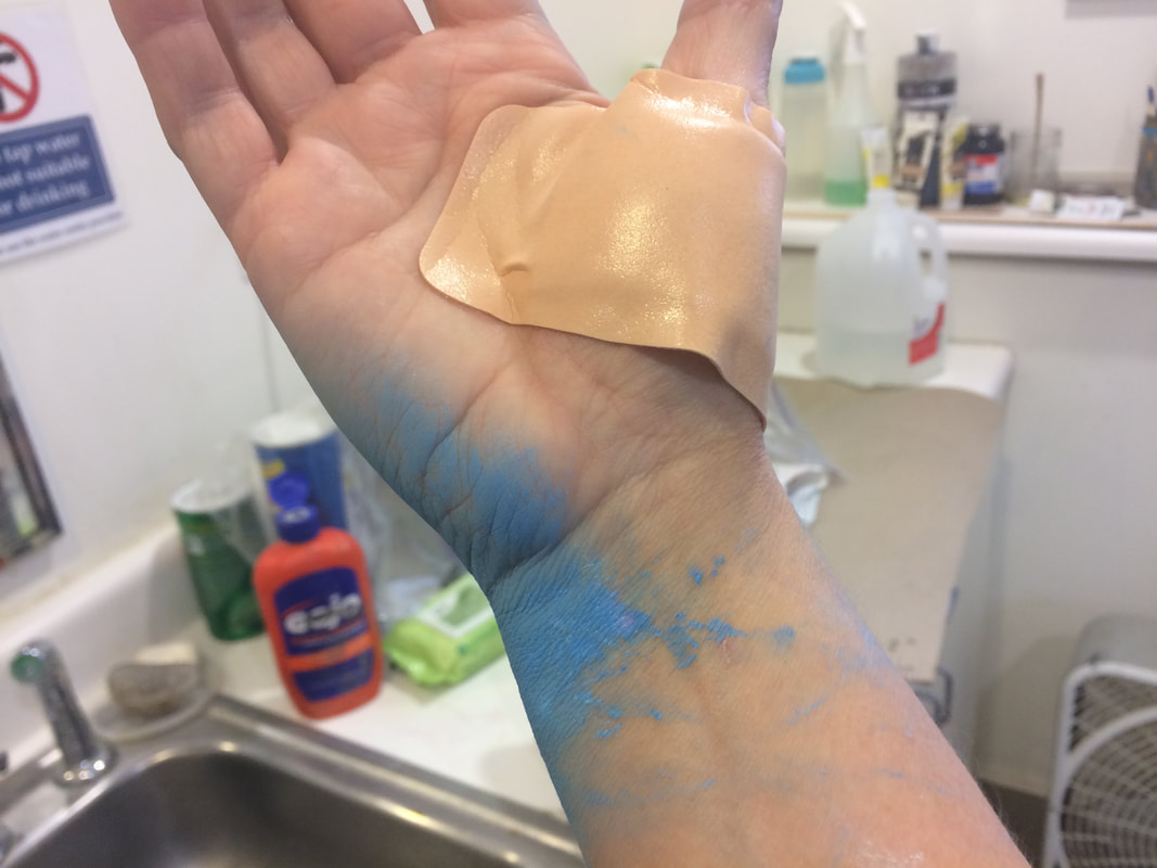 Image description - the palm side of a right hand with a large waterproof bandage at the base of the thumb, and smears of blue paint around the pinky side of the palm and down the wrist.